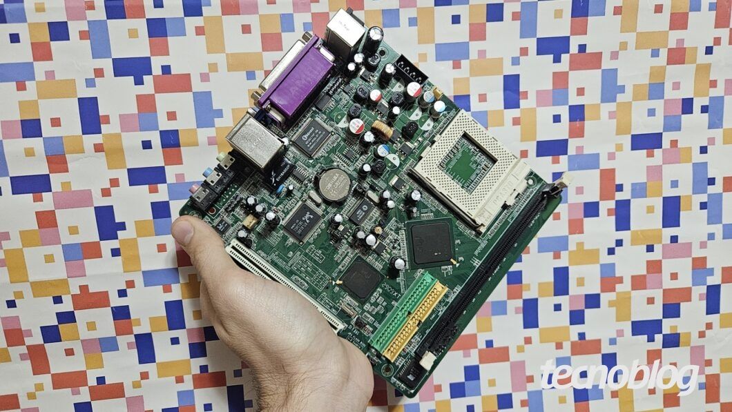 Mão segurando placa-mãe Mini-ITX; guia de compatibilidade com CPU, RAM e BIOS. Legenda da imagem. Reprodução: Retorno do item 11