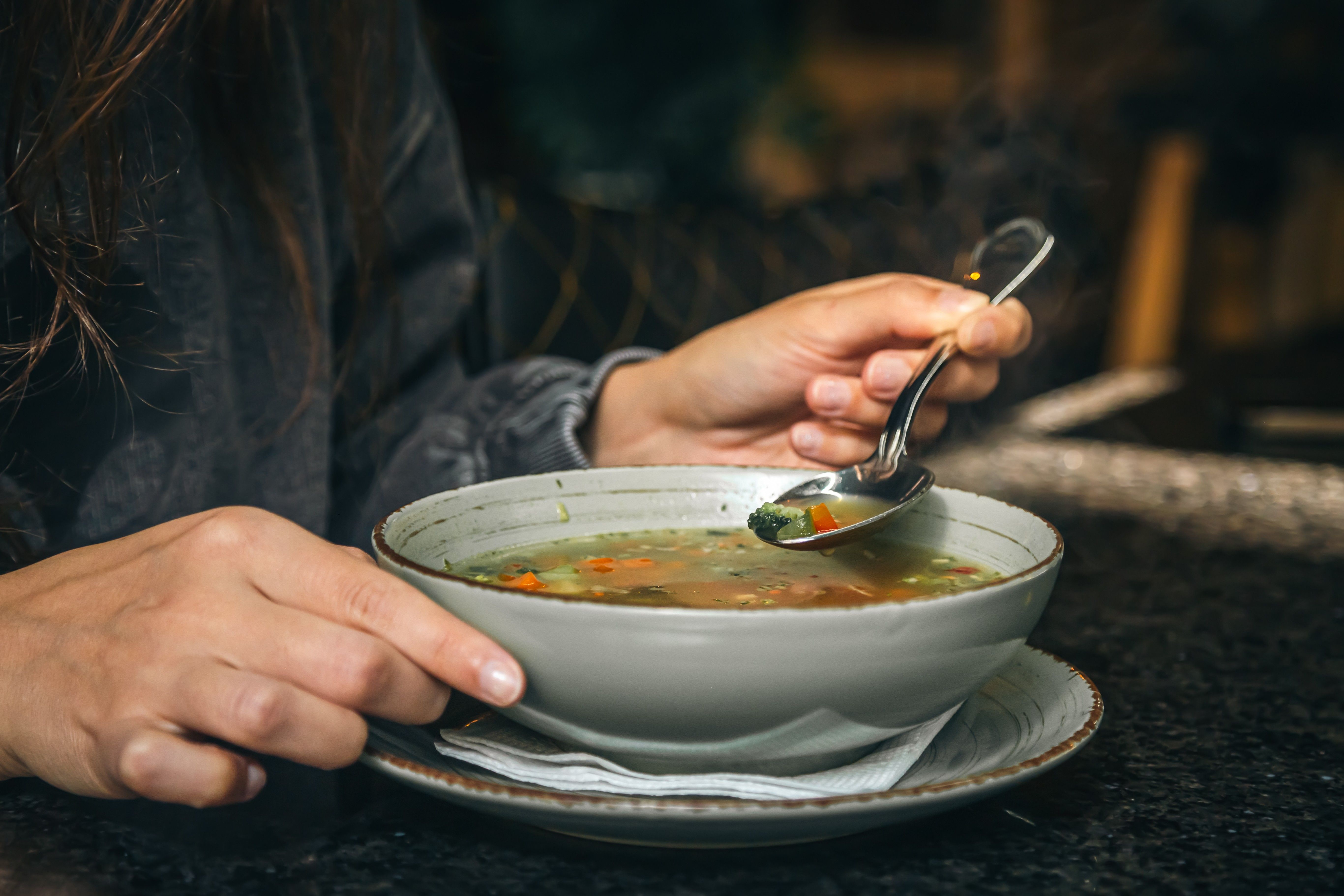 Mulher saboreia uma sopa de vegetais em café, destacando a importância da nutrição na prevenção de resfriados. Reprodução: Globo