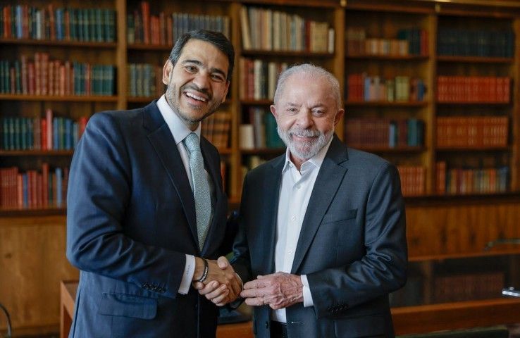 Lula e Jorge Messias apertam as mãos em ambiente formal com estantes ao fundo.
