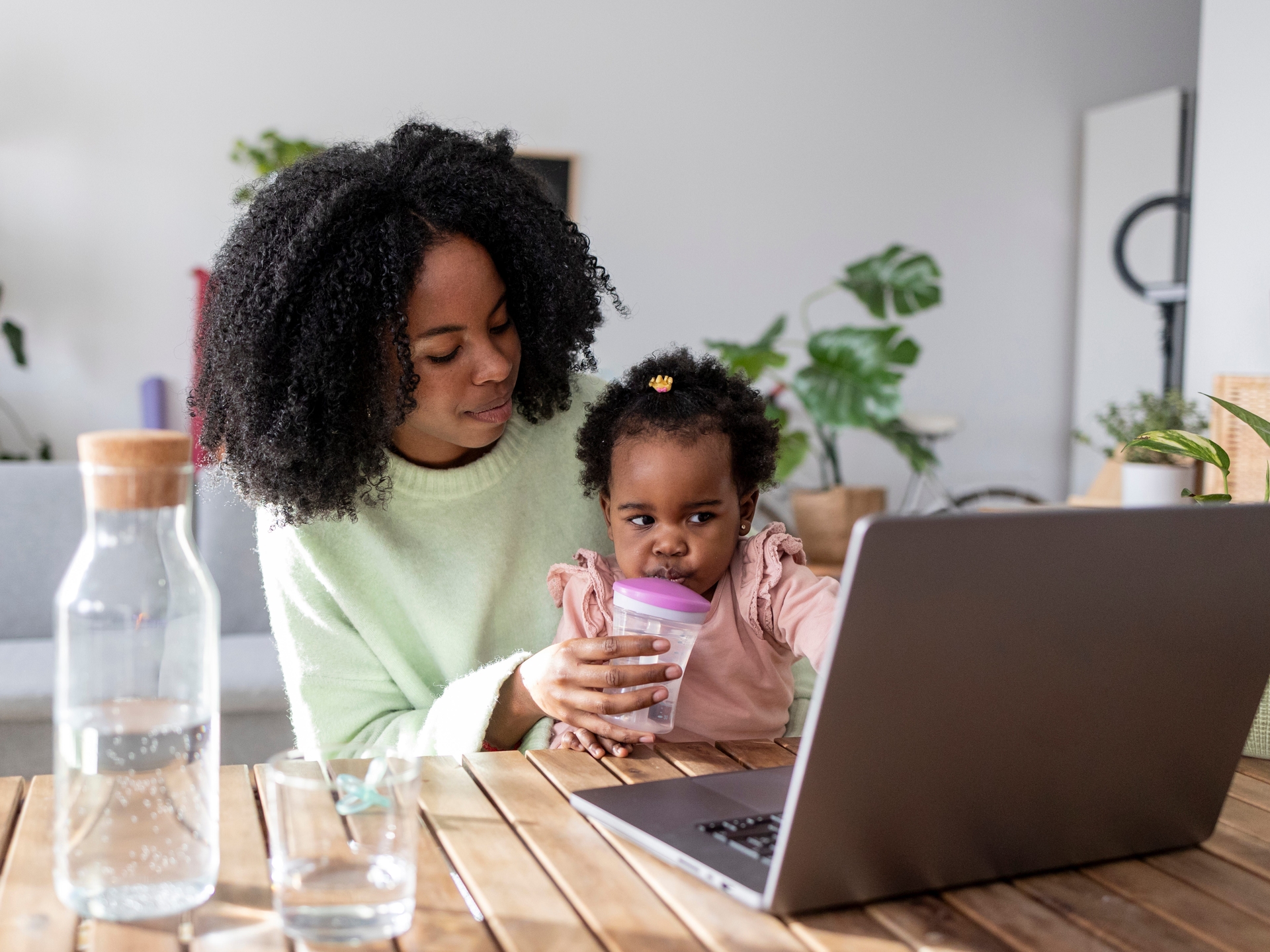 Mãe trabalhando no computador enquanto cuida de seu bebê, refletindo sobre os desafios da maternidade e carreira. Reprodução: Business Insider