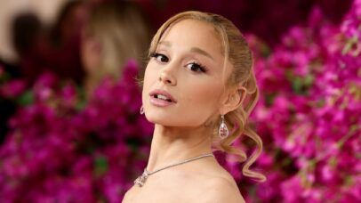 Ariana Grande posa elegante com fundo de flores rosas vibrantes.