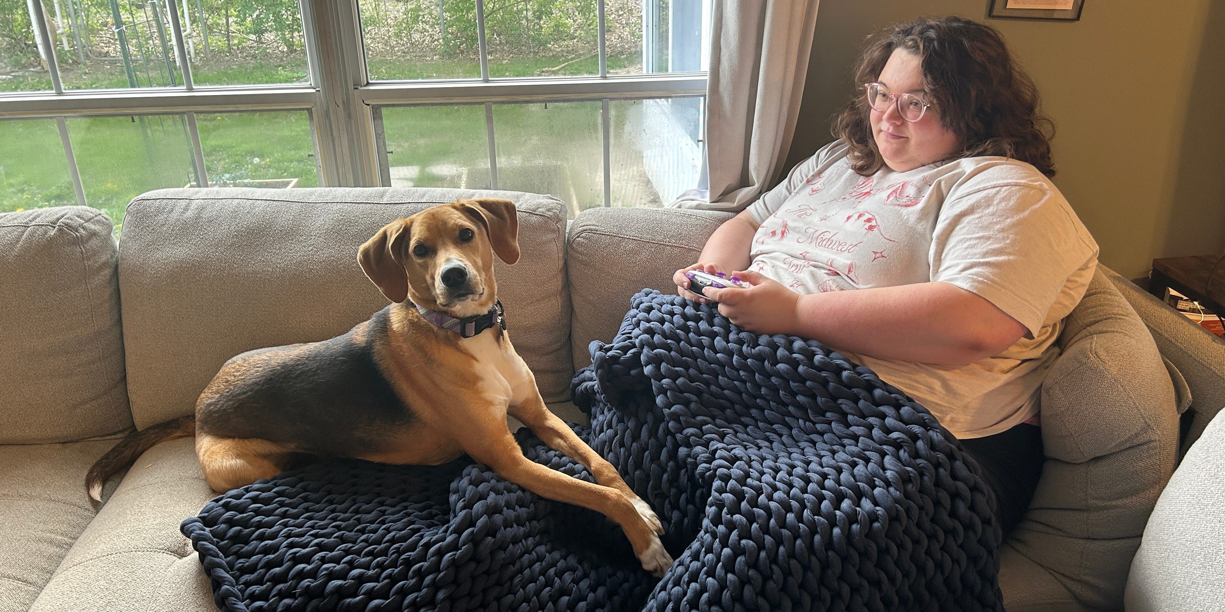 Mulher e cachorro relaxam no sofá com um cobertor ponderado azul. Reprodução: Business Insider