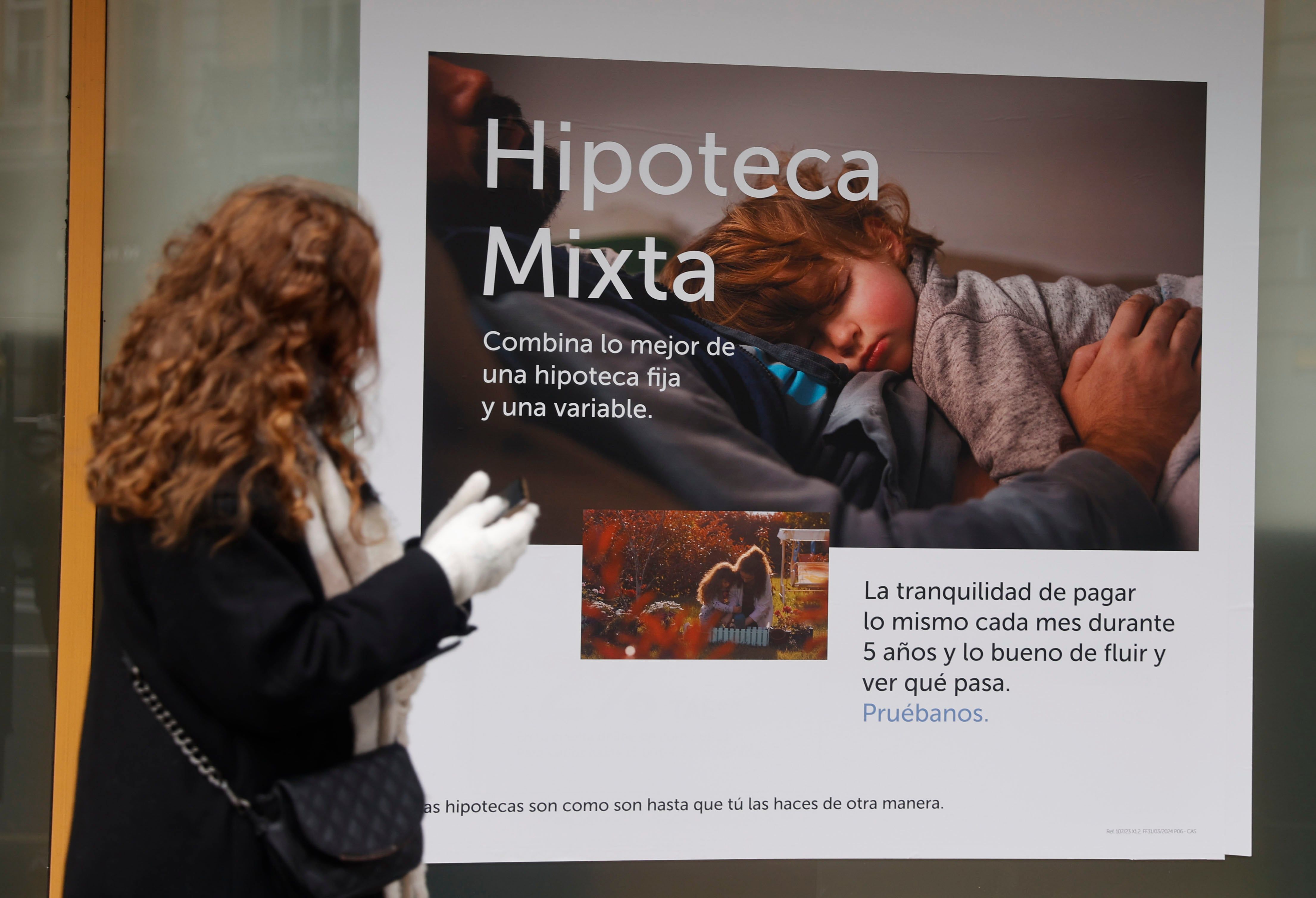 Mulher passa por anúncio de hipoteca enquanto busca taxas mais baixas entre bancos. Legenda da imagem. Reprodução: Cinco Dias