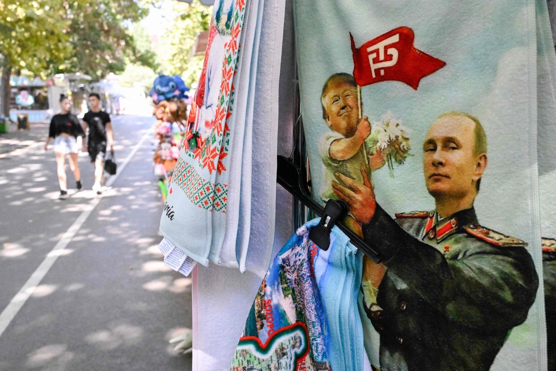 Turistas passam por um stand de toalhas com imagem de Vladimir Putin em contexto da guerra na Ucrânia. Reprodução: Globo