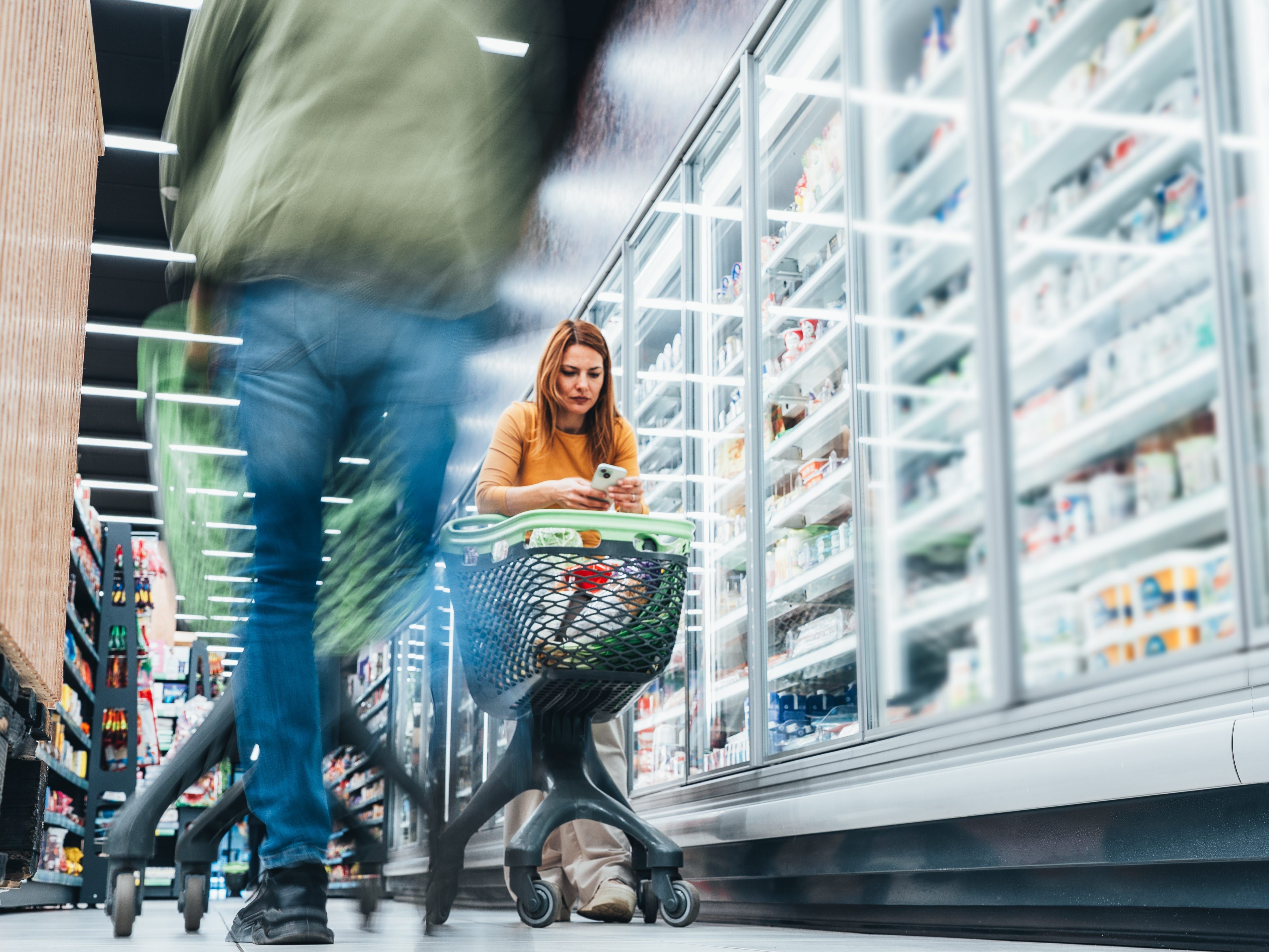 Mulher analisa ofertas e cupons enquanto faz compras no supermercado.; Legenda da imagem. Reprodução: Business Insider