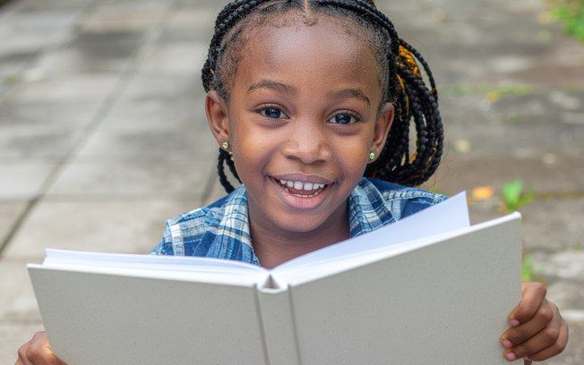 Criança sorridente segura livro aberto, simbolizando o prazer da leitura na infância.