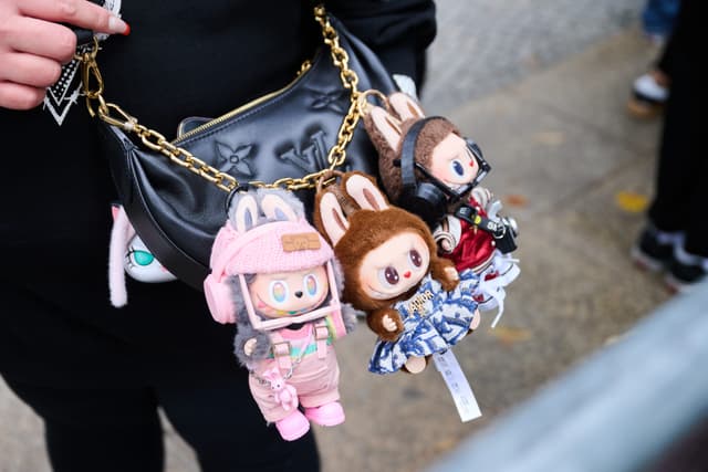 Mulher exibe bonecos Labubu pendurados na bolsa, em fila na KaDeWe. Legenda da imagem. Reprodução: Retorno do item 11