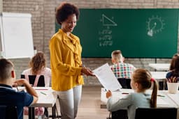 Professora entrega resultados de prova a estudante em sala de aula. Reprodução: Retorno do item 11