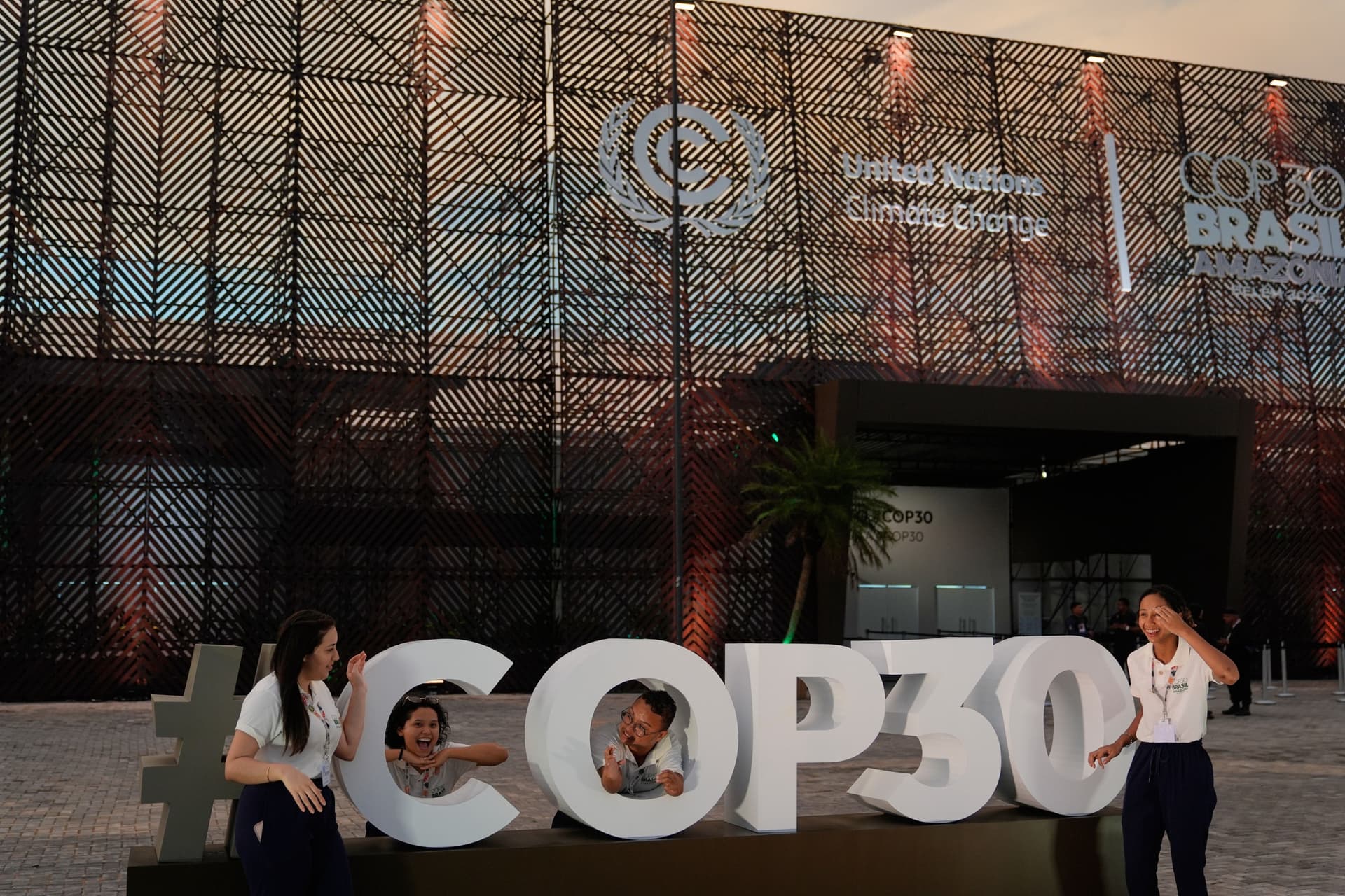 Pessoas posam diante do local da COP30 em Belém, início da conferência climática da ONU. Legenda da imagem. Reprodução: Retorno do item 11