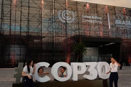 Pessoas posam diante do local da COP30 em Belém, início da conferência climática da ONU. Legenda da imagem. Reprodução: Retorno do item 11