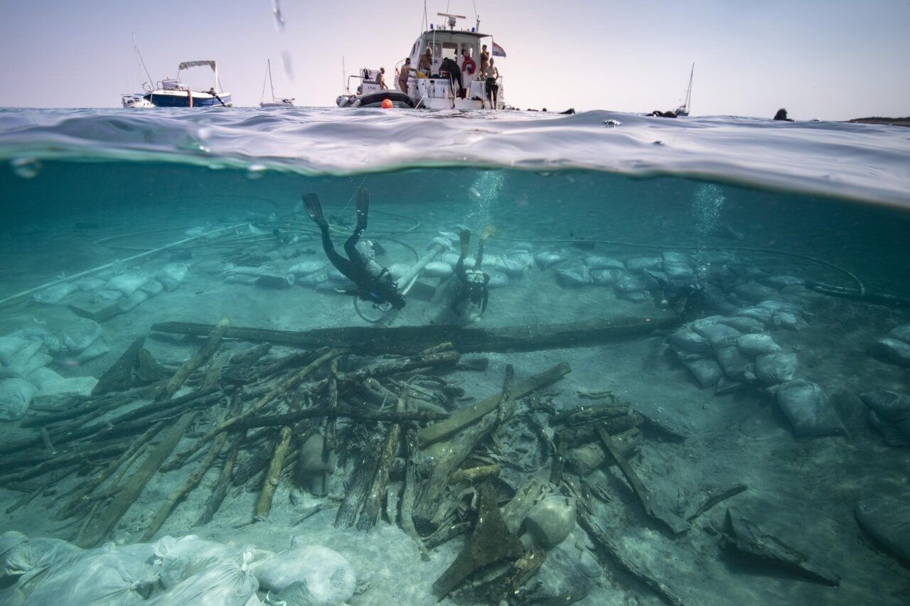 [Marinheiros romanos consertam navio à beira-mar, longe de casa.]. Reprodução: Gizmodo