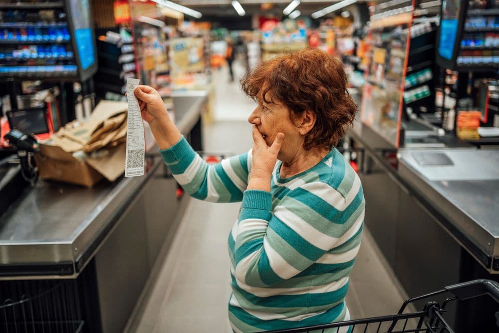 Mulher idosa examina um recibo em supermercado, alerta sobre bisfenóis perigosos. Legenda da imagem. Reprodução: Business Insider