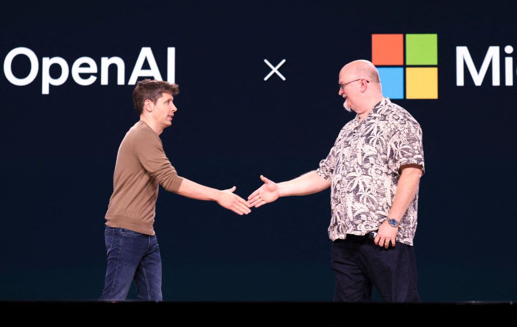 Executivos da OpenAI e Microsoft apertam as mãos em evento de parceria tecnológica.