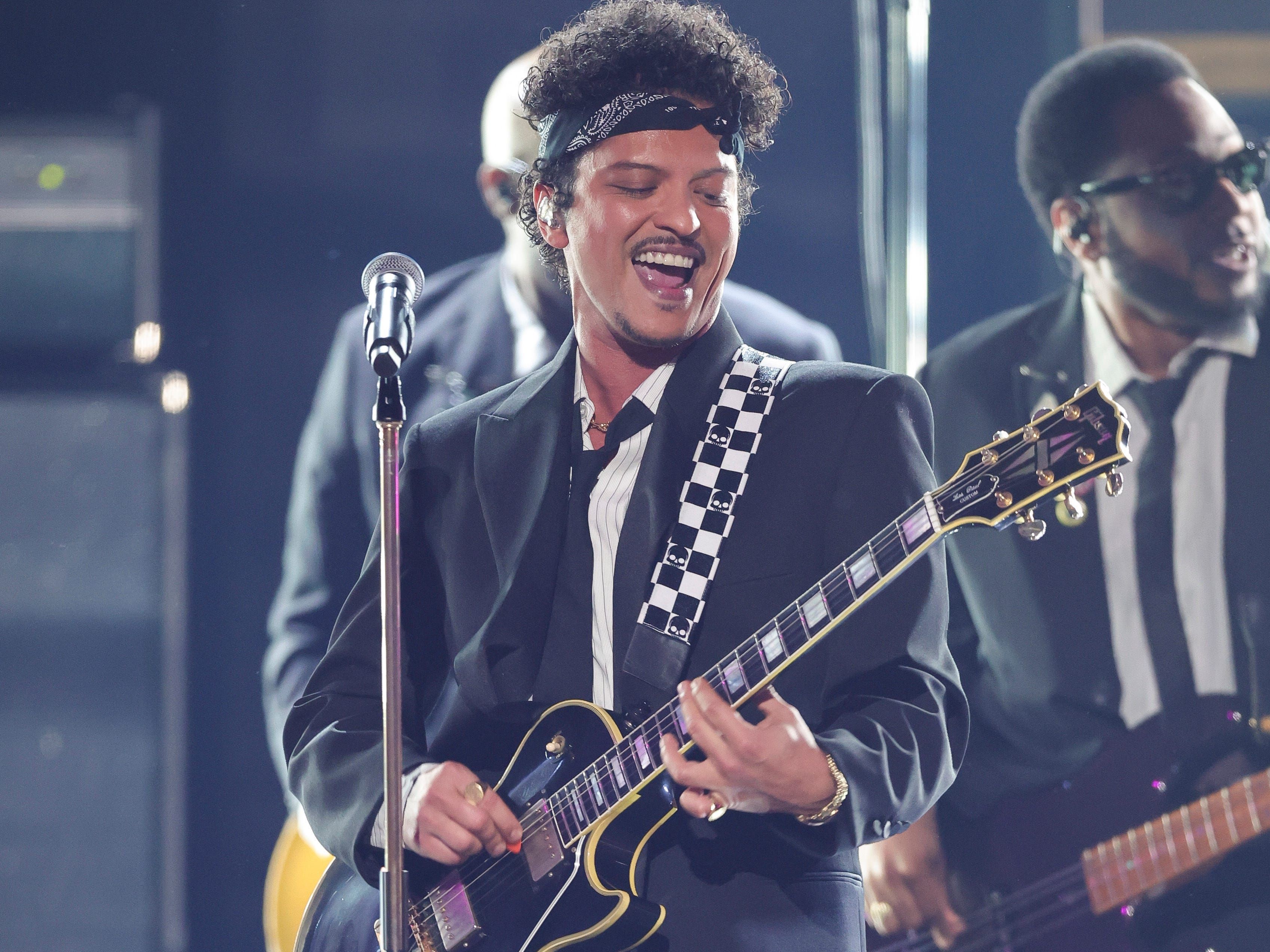 Bruno Mars toca guitarra e canta animado durante apresentação ao vivo.