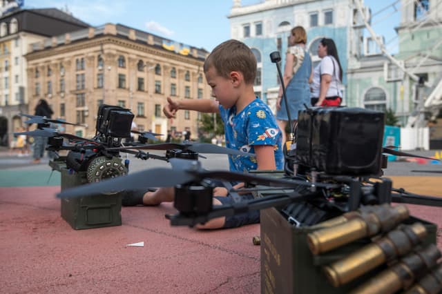 Menino observa drone FPV em exposição; doações civis abastecem unidades ucranianas. Legenda da imagem. Reprodução: Business Insider