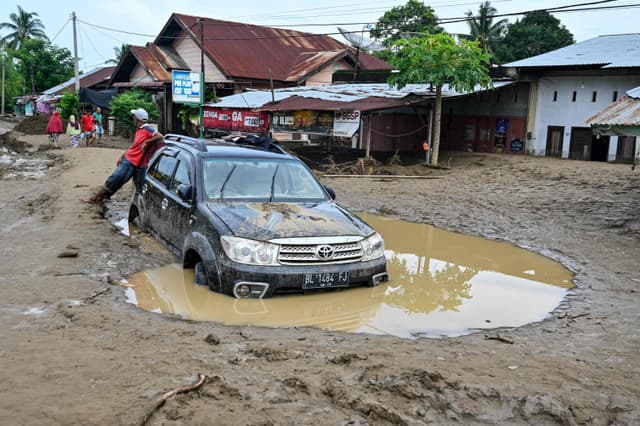 Homem ao lado de carro preso na lama após enchente rápida em Meureudu, Indonésia.. Reprodução: Oglobo