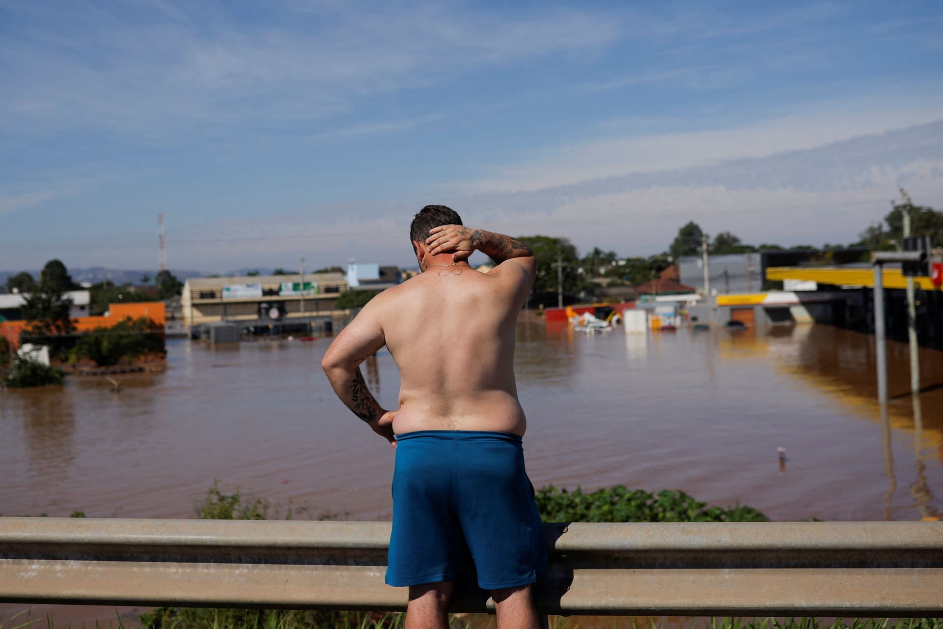 Homem observa região alagada no RS, refletindo impactos climáticos e saúde mental. Reprodução: Globo
