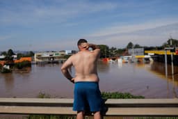 Homem observa região alagada no RS, refletindo impactos climáticos e saúde mental. Reprodução: Globo