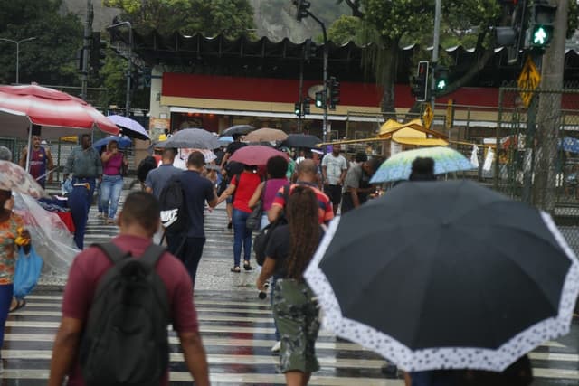 Pessoas enfrentam chuva fraca no centro do Rio de Janeiro, alertando para clima instável na região. Reprodução: Globo